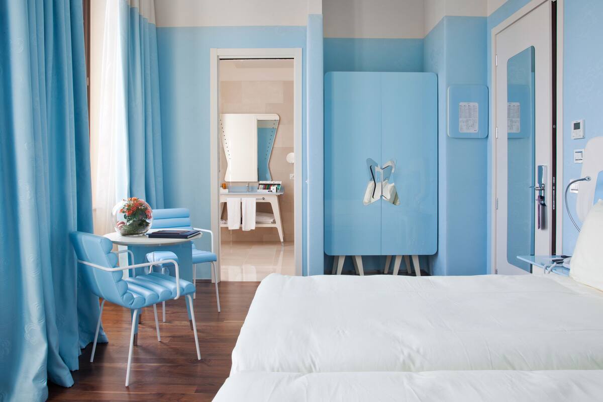 A hotel room with a bed, a desk with a chair, a bathroom with a mirror, and a wardrobe.