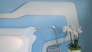 Una cama con ropa de cama blanca, un cabezal de ducha y un pequeño arreglo floral blanco en un florero.
