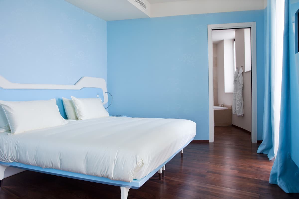 A bedroom with a bed, a bathroom visible through an open door, and a blue curtain.