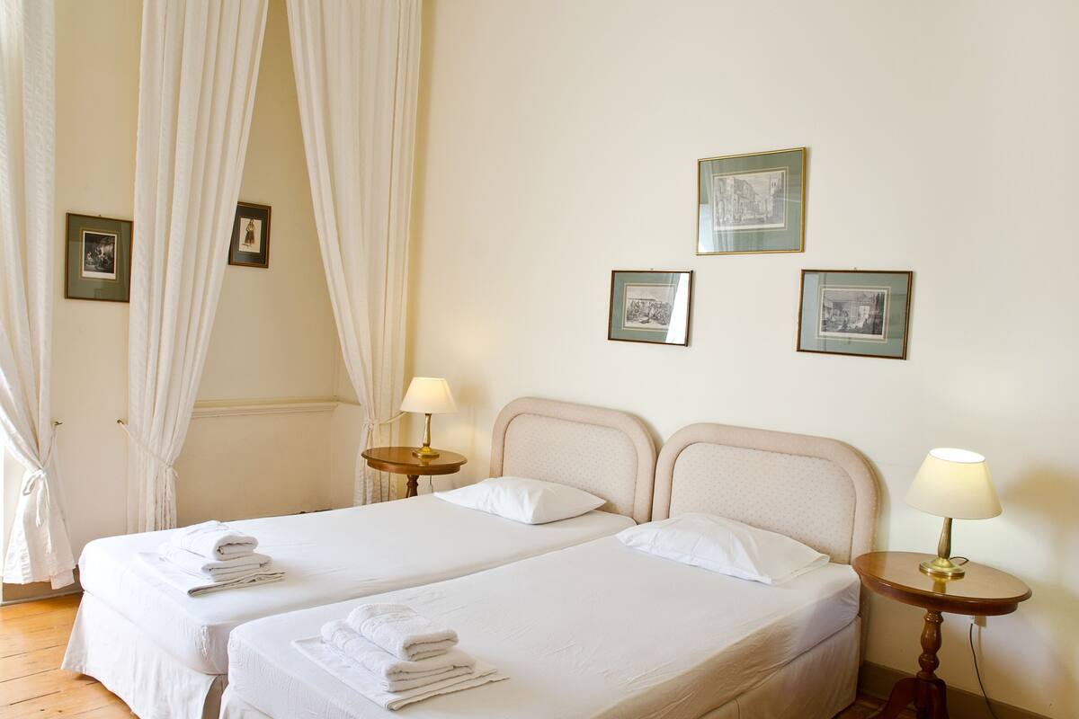 A hotel room with two beds, a nightstand with a lamp, and three framed pictures on the wall.