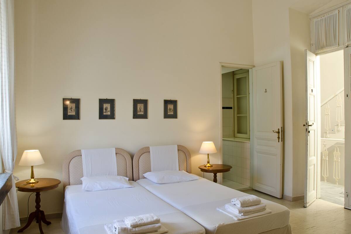 A double bed with white linens, two bedside tables with lamps, and a door leading to a bathroom.