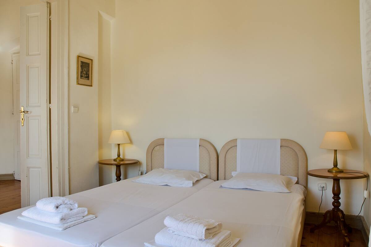 A hotel room with two beds, white linens, and towels. There are bedside tables with lamps.