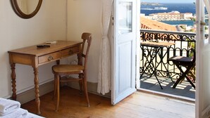 Una stanza con una scrivania in legno, una sedia e un letto. C’è un televisore montato a parete e una finestra con tende.