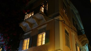 Un edificio con un cartello che riporta "Hotel Omicron". Presenta una facciata in pietra, un balcone con ringhiere e un ingresso con tappetino.