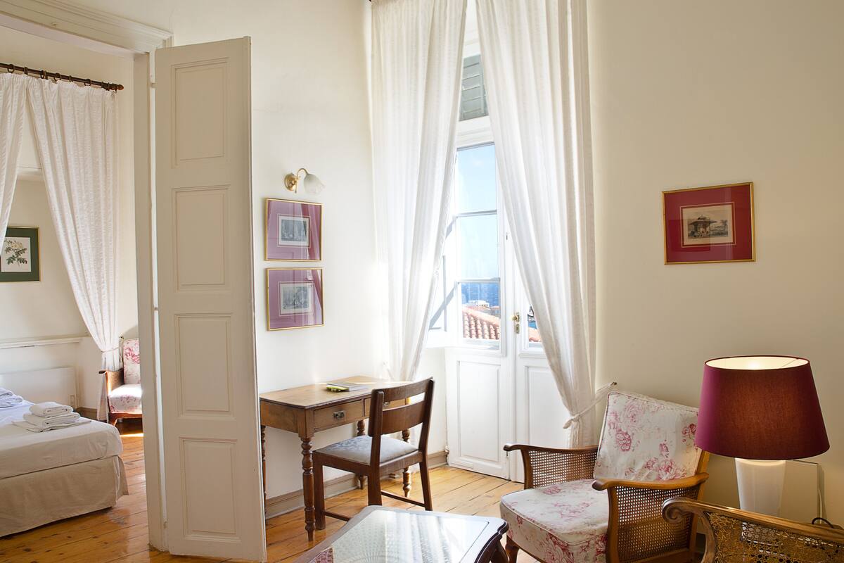 A room with a bed, a desk, a chair, a table, and a lamp.