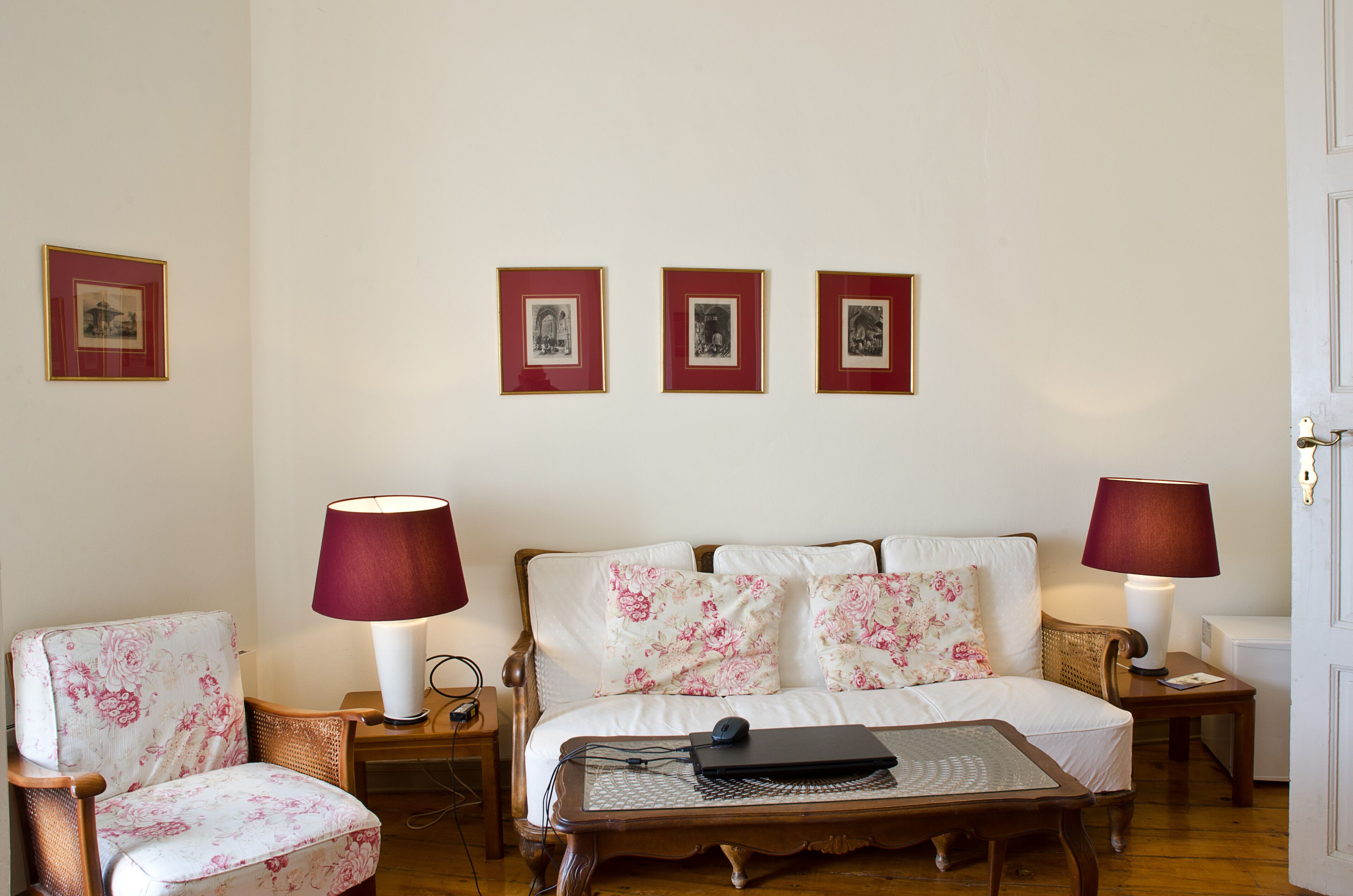 A room with a bed, two chairs, a table, and three framed pictures on the wall.