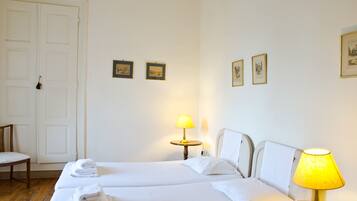 Una habitación de hotel con dos camas, una silla, una lámpara y cuadros en la pared.