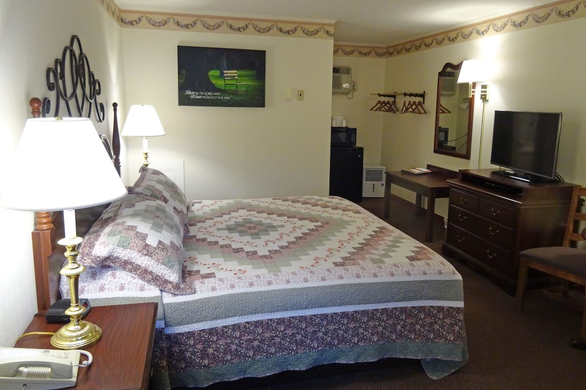 A hotel room with a bed, a desk, a dresser, a television, and a wall-mounted air conditioner.