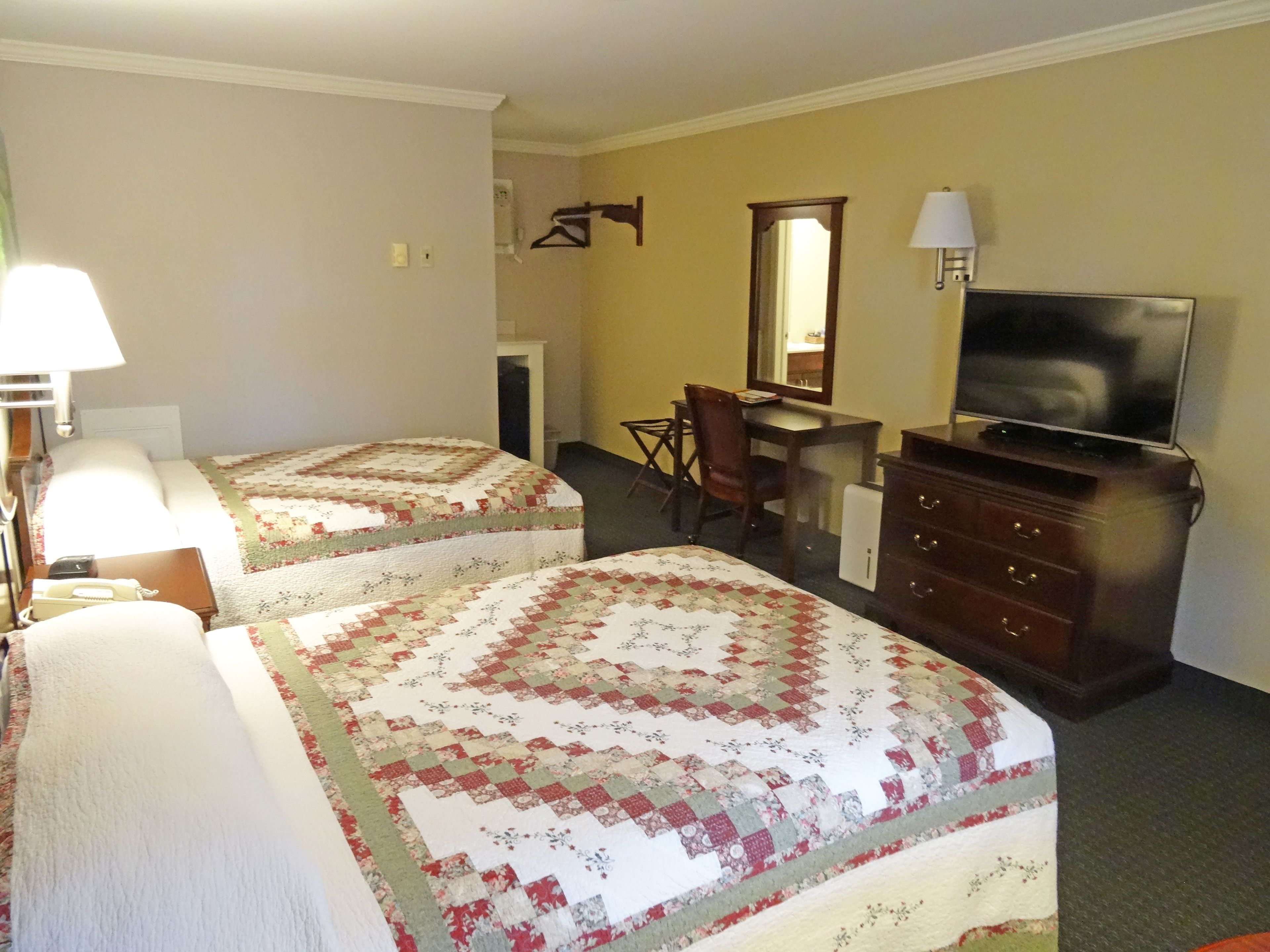 A hotel room with two beds, a desk, a chair, a dresser, a TV, and a lamp.