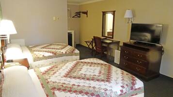 A hotel room with two beds, a desk, a chair, a dresser, a TV, and a lamp.