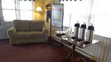 A living room with a sofa, a table with thermos flasks, a framed menu, and a trash bin.