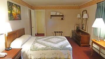 Habitación de hotel con cama, mesita de noche, lámpara, cómoda, espejo y un cuadro en la pared.