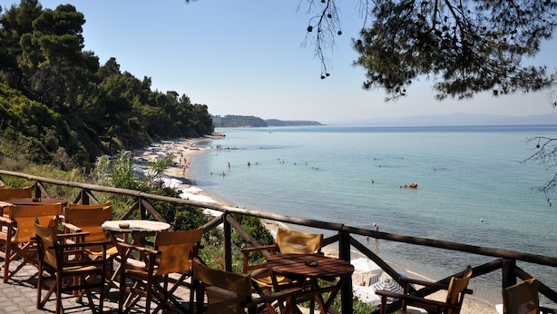 A seaside terrace with wooden chairs and tables, overlooking a beach and calm sea. - Hotel Pighi (Kassandra)