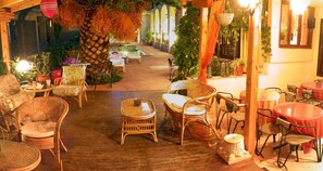 An outdoor seating area with wicker furniture, a stone pillar, and hanging plants. - Hotel Pighi (Kassandra)