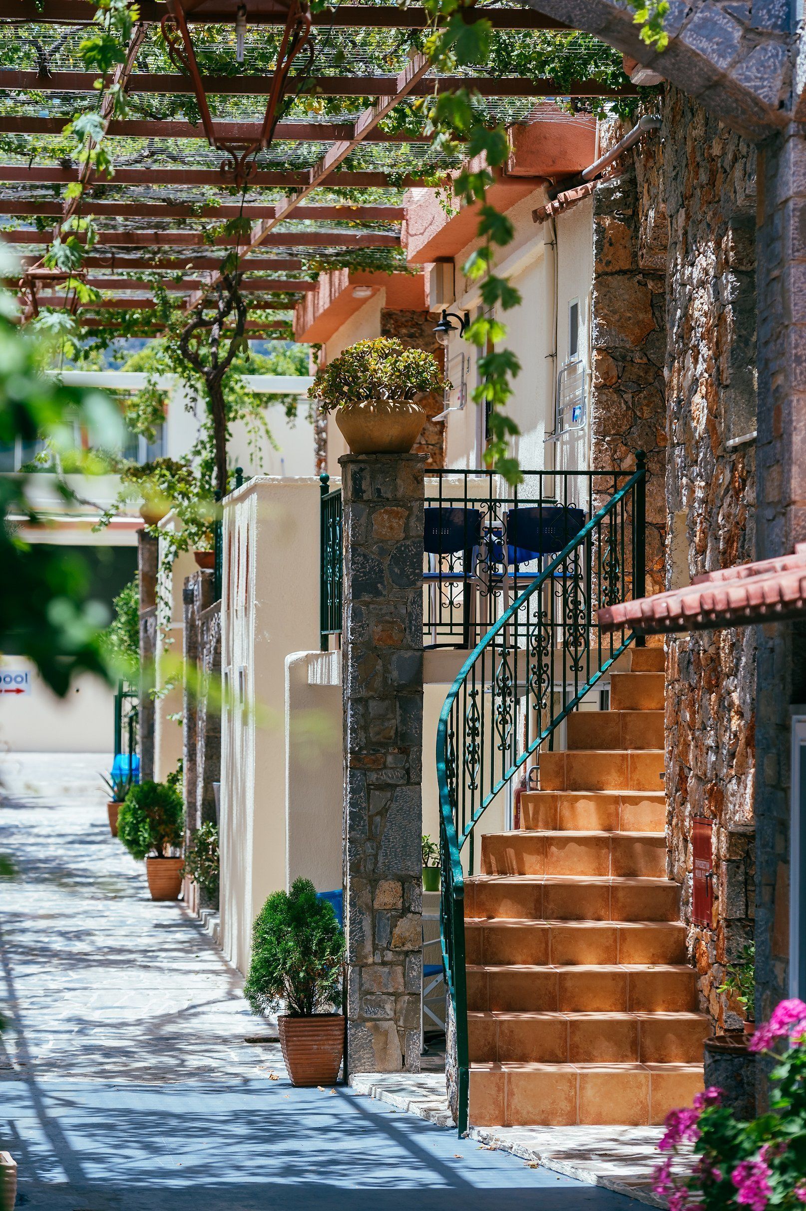 A narrow street with stone buildings, a staircase with a green railing, and potted plants along the path.