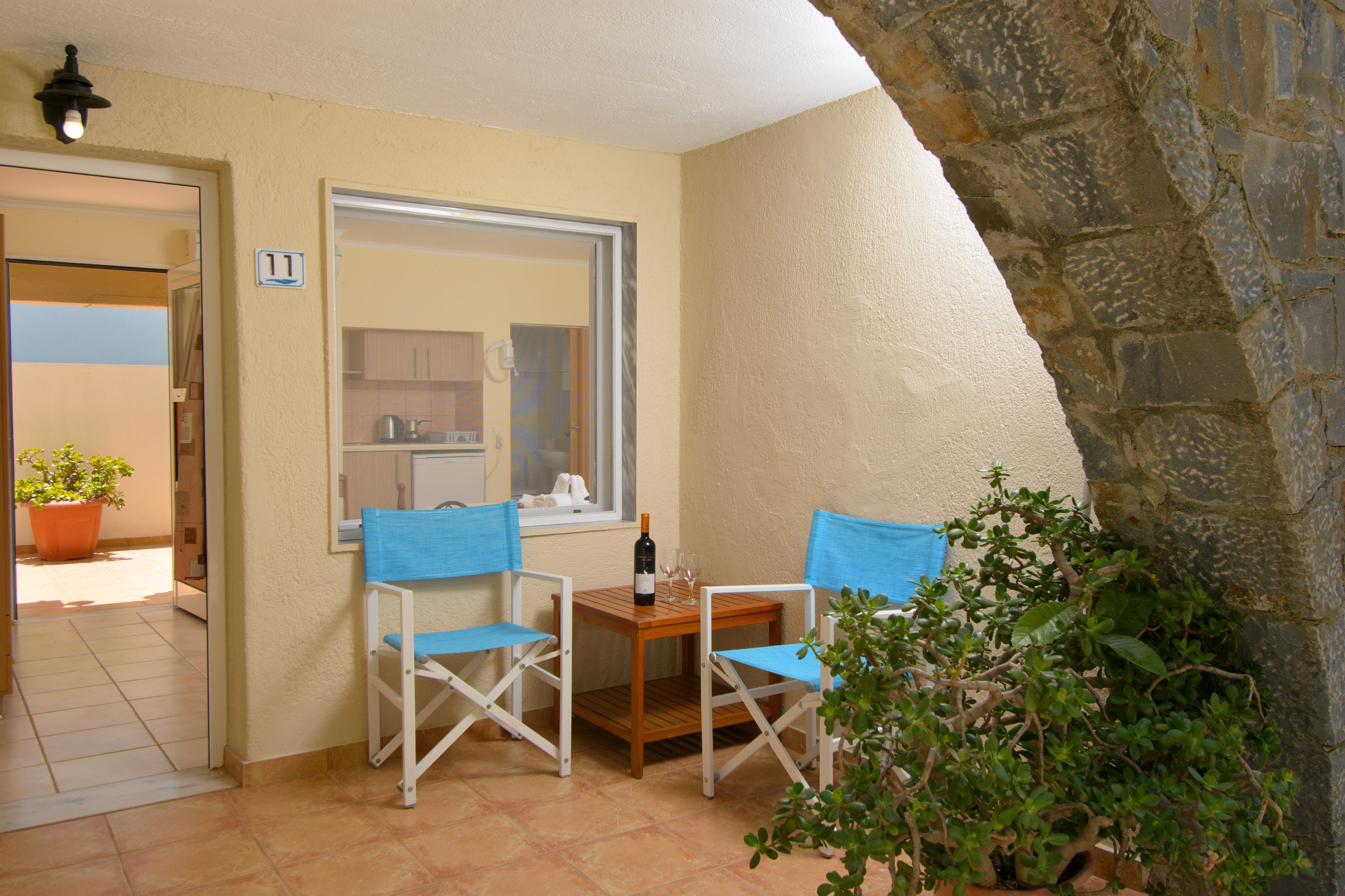 A small patio with two blue chairs, a wooden table, and a bottle of wine.