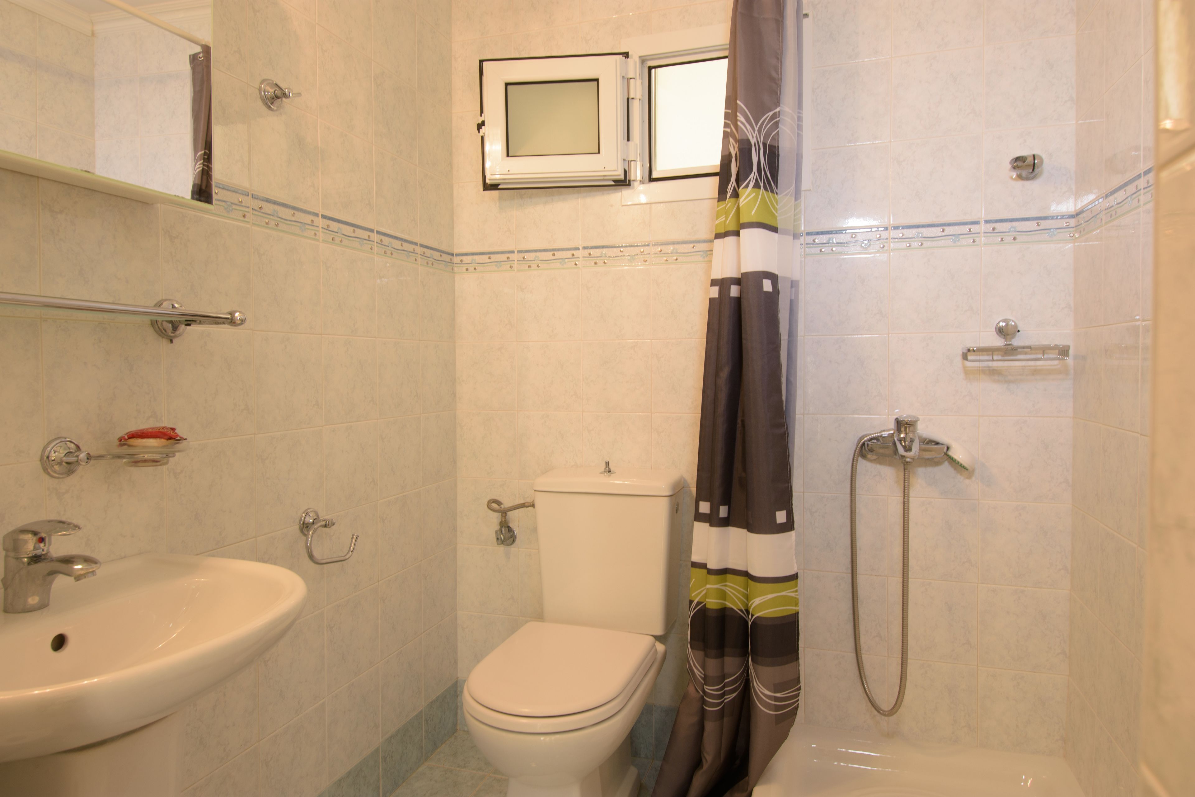 Un bagno con WC, lavandino, doccia e una piccola finestra.