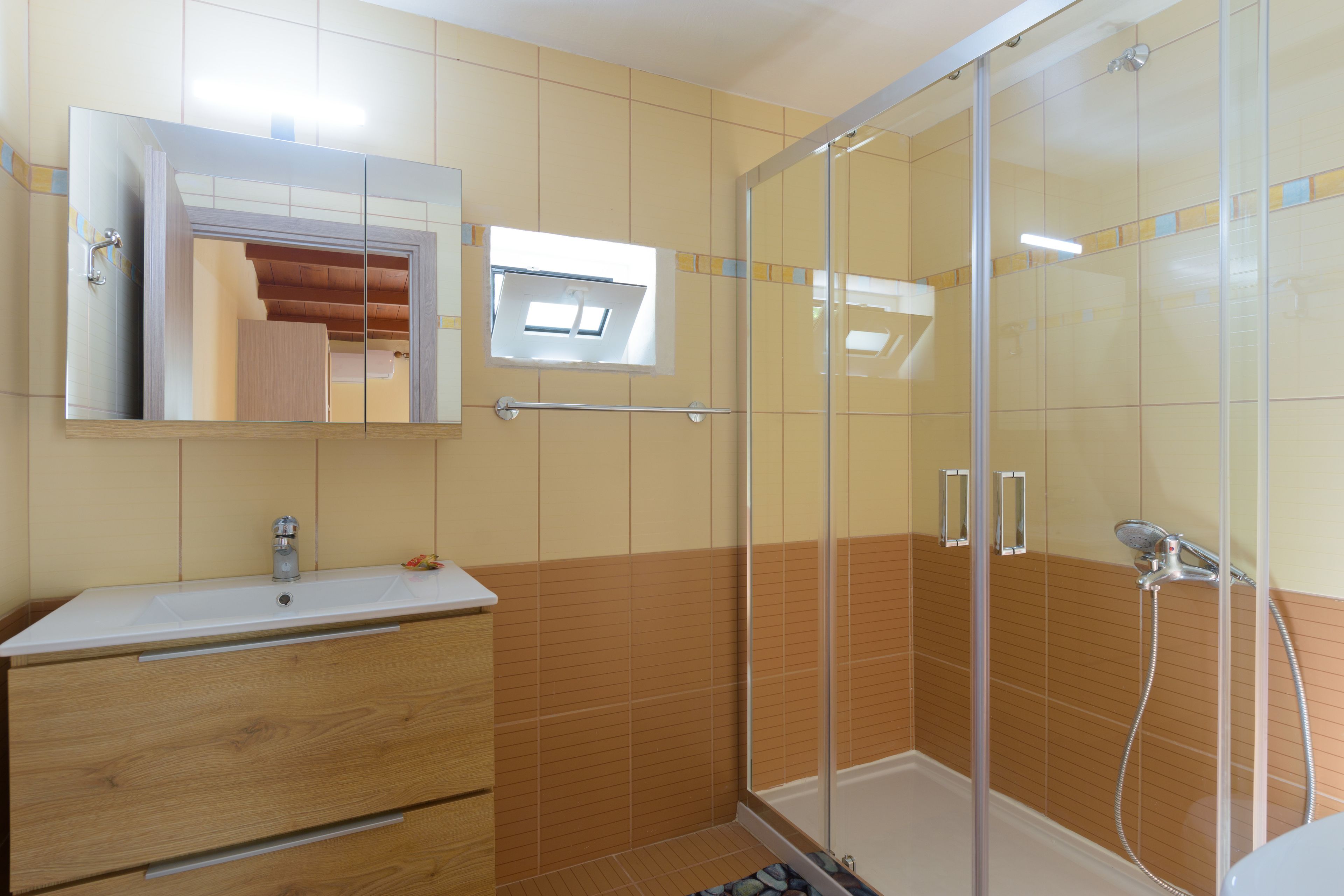 A bathroom with a glass shower enclosure, a wooden vanity with drawers, and a mirror above the sink.