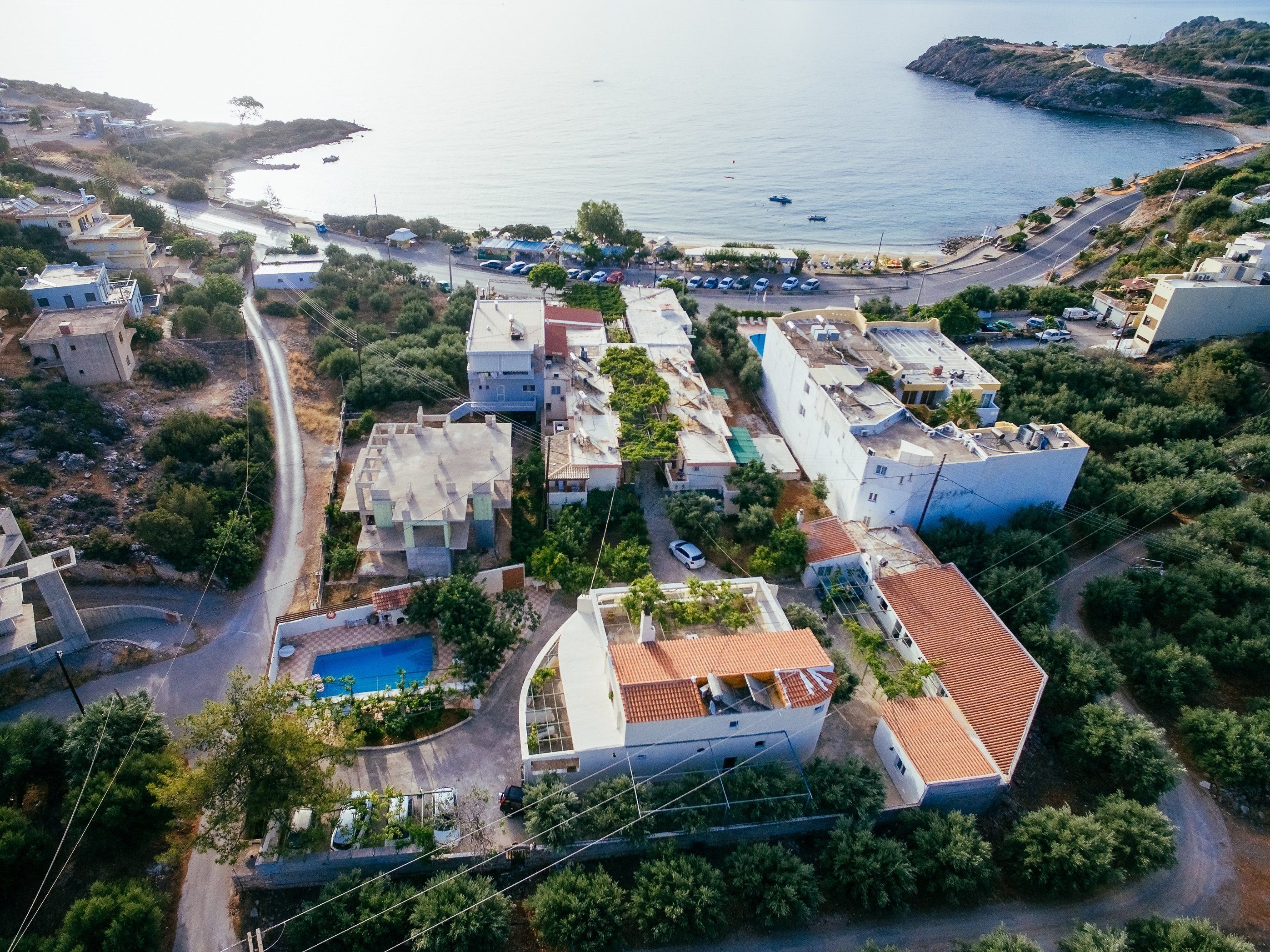 An aerial view of a coastal residential area with houses, a swimming pool, and a road leading to the beach.