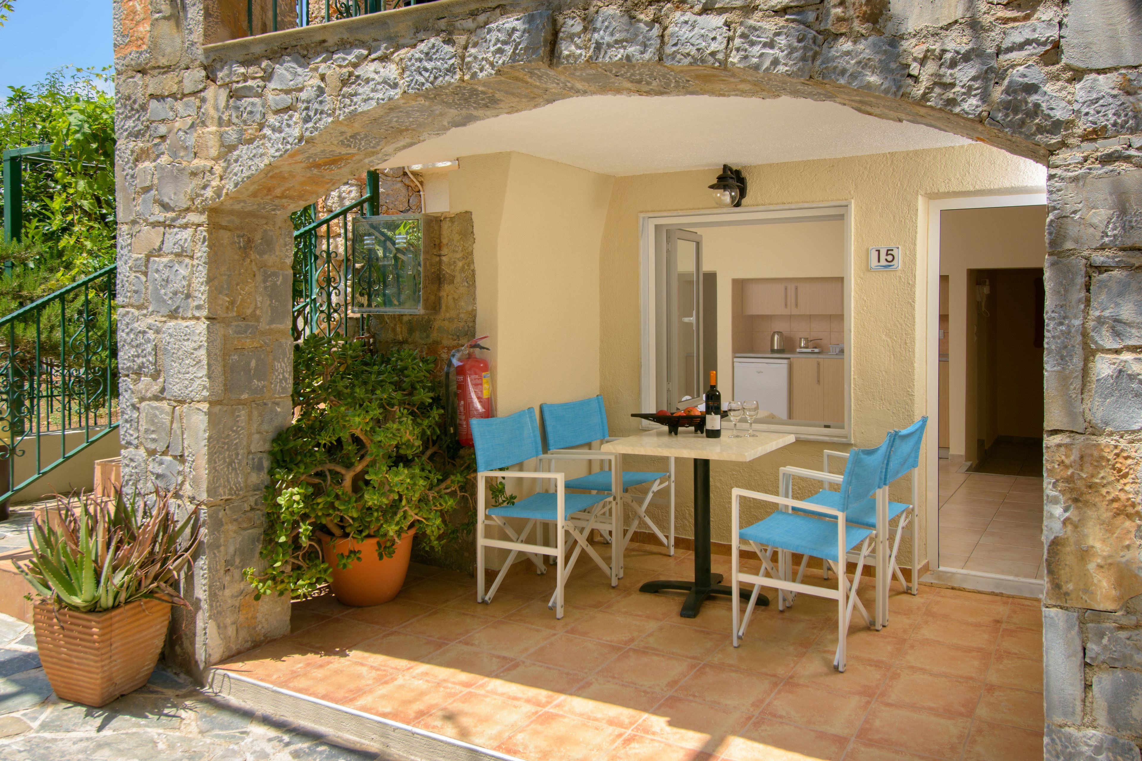 Un arco de piedra que da acceso a un patio con una mesa y sillas, una planta en maceta y vistas a una habitación con cocina.