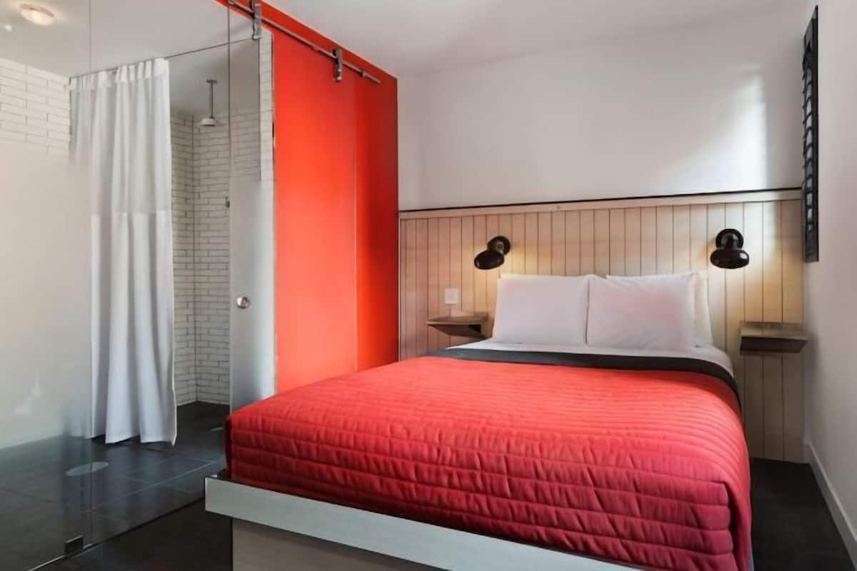 Une chambre moderne avec un grand lit, un espace douche et une tête de lit en bois.