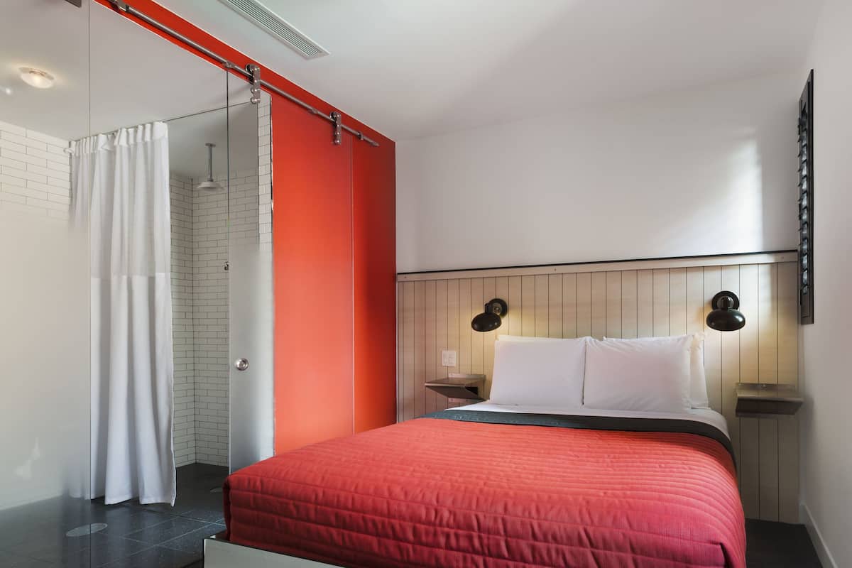 Une chambre à coucher moderne avec une couvre-lit rouge, des rideaux blancs et une tête de lit en bois.