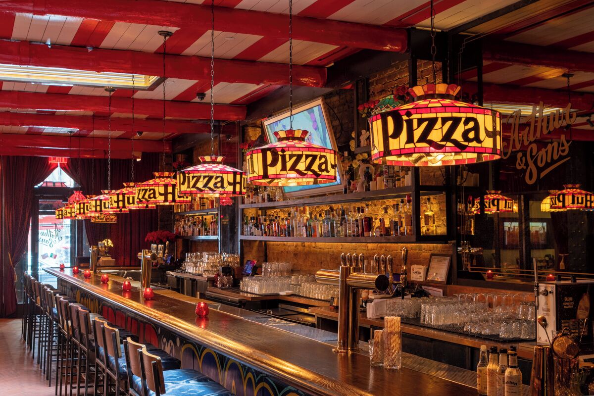 En bar med flere hængende pizzalys, hylder fyldt med flasker og en lang bardisk med skamler.