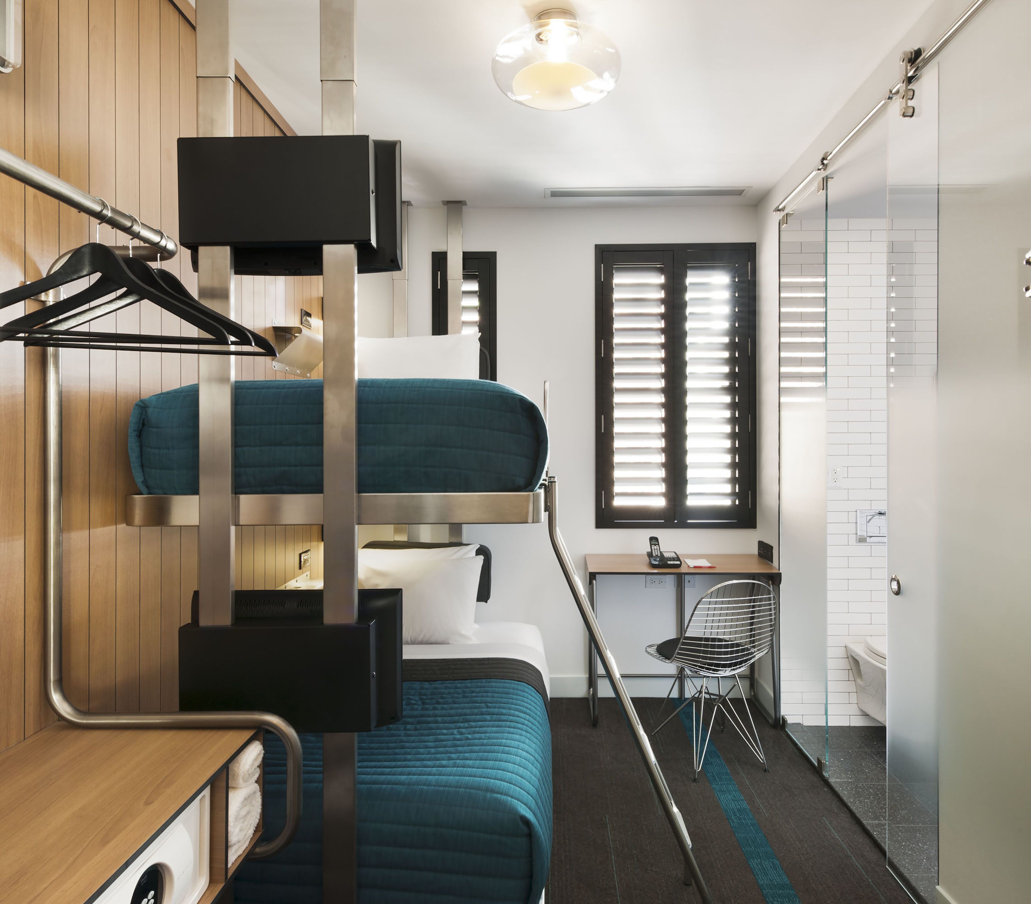 Habitación de hotel compacta y moderna con literas, escritorio y zona de ducha.