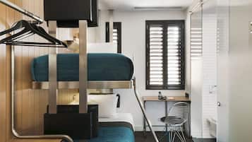 Habitación de hotel compacta y moderna con literas, escritorio y zona de ducha.