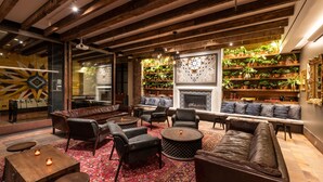 A cozy lounge area with leather sofas, round tables, and a fireplace.