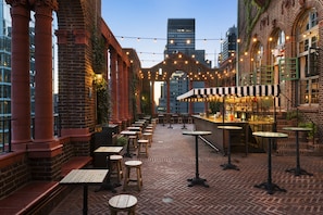 An outdoor patio with brick flooring, wooden tables and stools, and string lights.