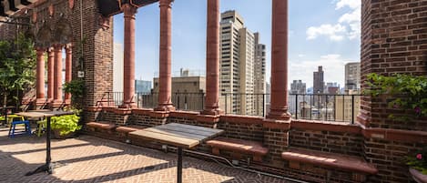 Una terraza en la azotea con columnas de ladrillo, una mesa de madera y vistas del horizonte urbano.