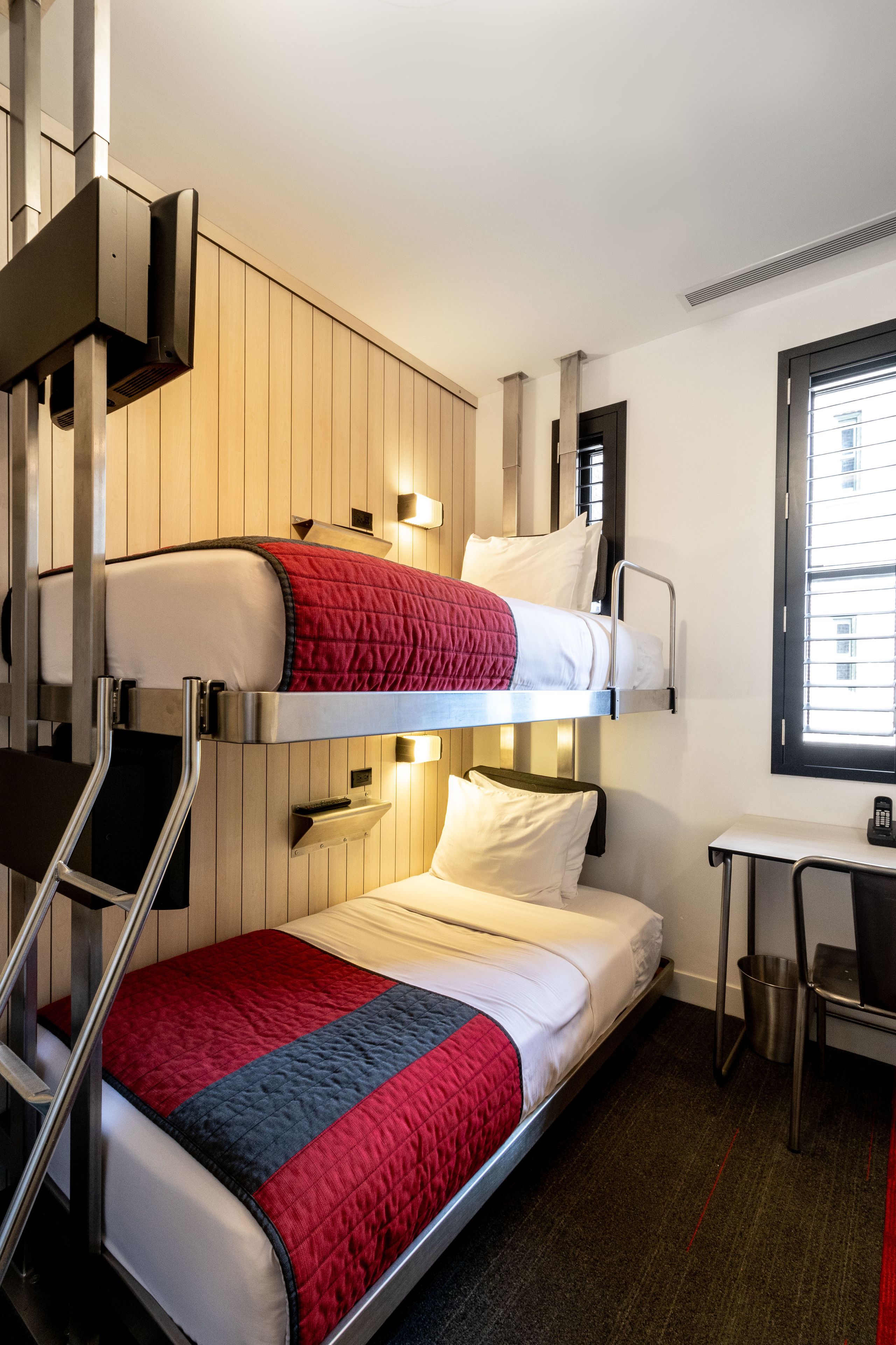 A bunk bed room with a desk and chair, a window, and a wall-mounted heater.