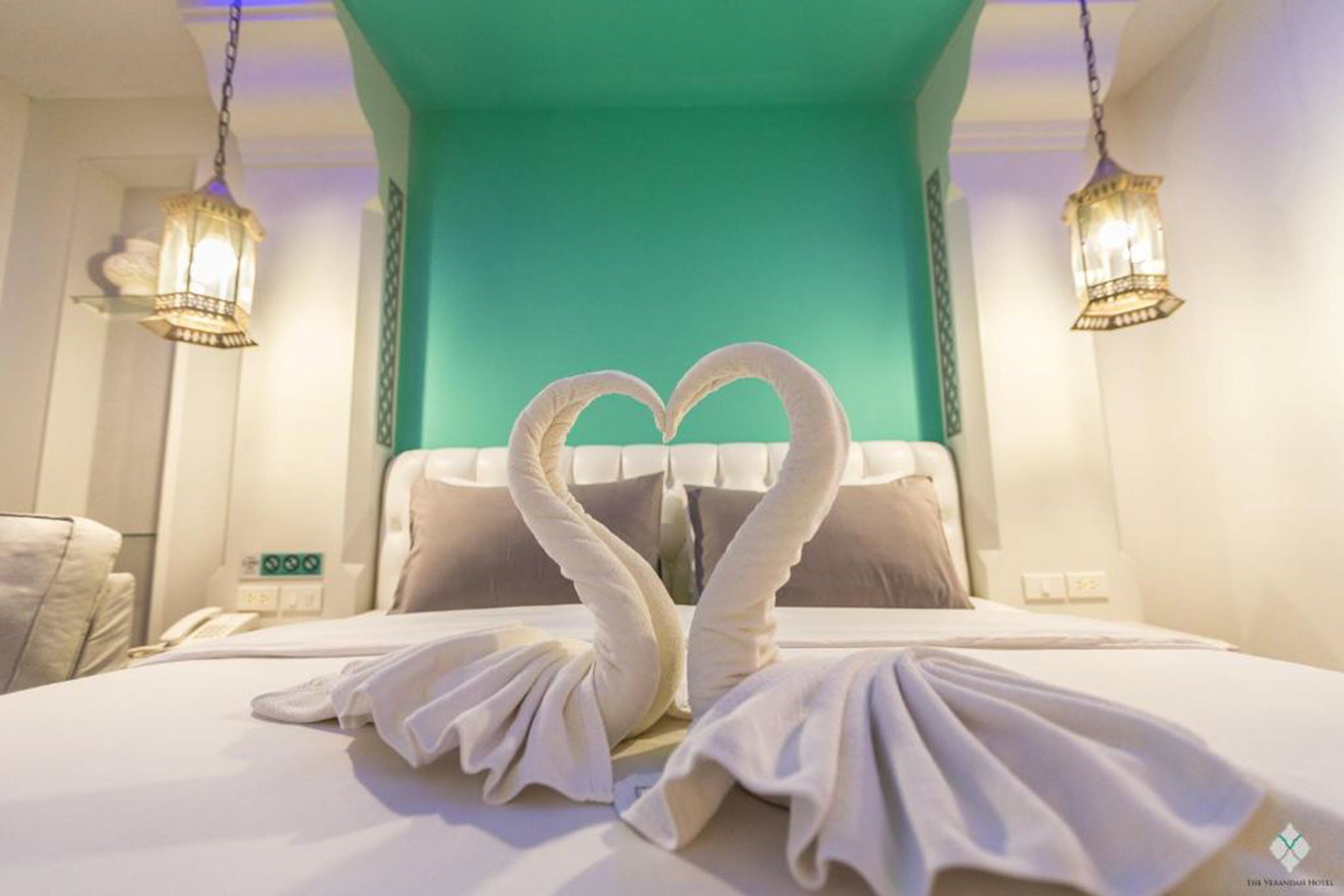 A hotel room with a bed, two wall-mounted lamps, and a teal-colored wall.