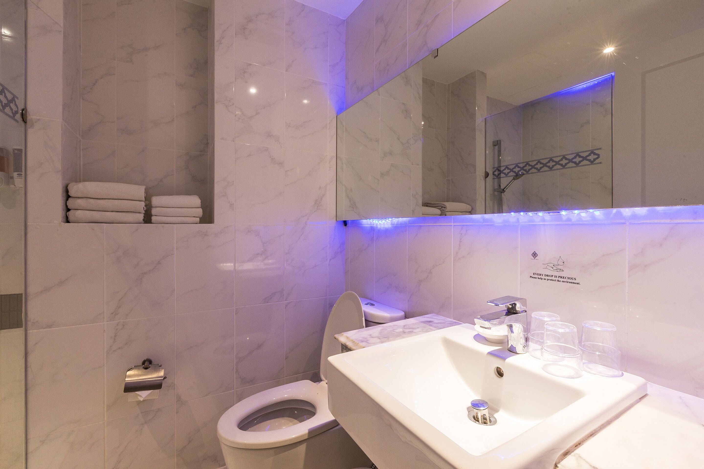 A modern bathroom with a marble floor, a white sink with glass containers, a toilet, and a glass shower enclosure.