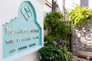 Une enseigne pour l’hôtel The Verandah, avec une arche décorative et un mur de pierre orné de plantes.