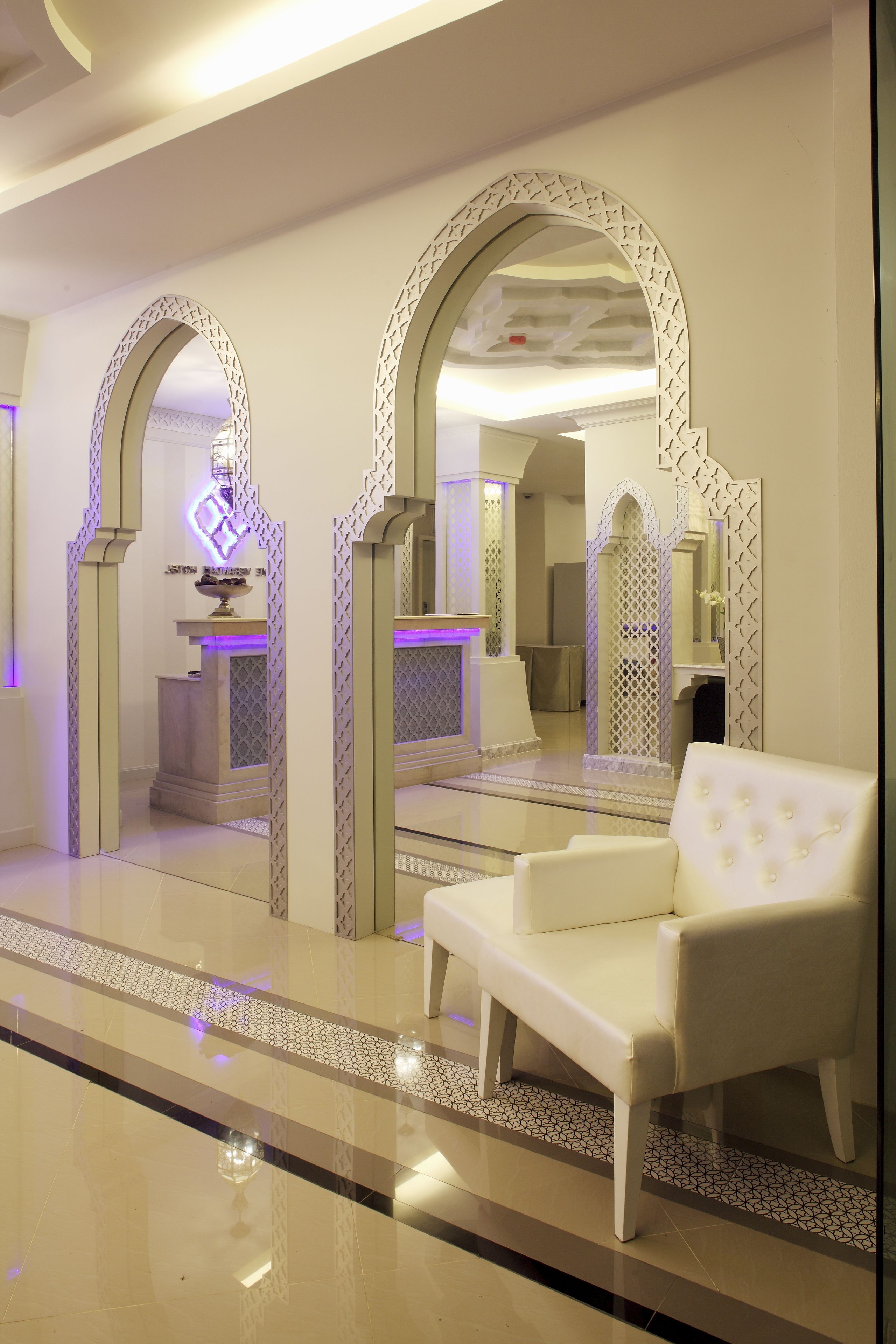 Un moderno vestíbulo de hotel con un sofá blanco, arcos decorativos y un suelo reflectante.