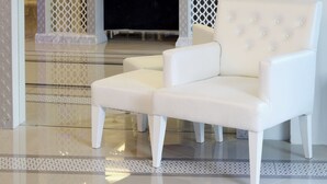 A white armchair in a room with a large mirror, ornate white lattice panels, and a chandelier. - The Verandah (Krabi)