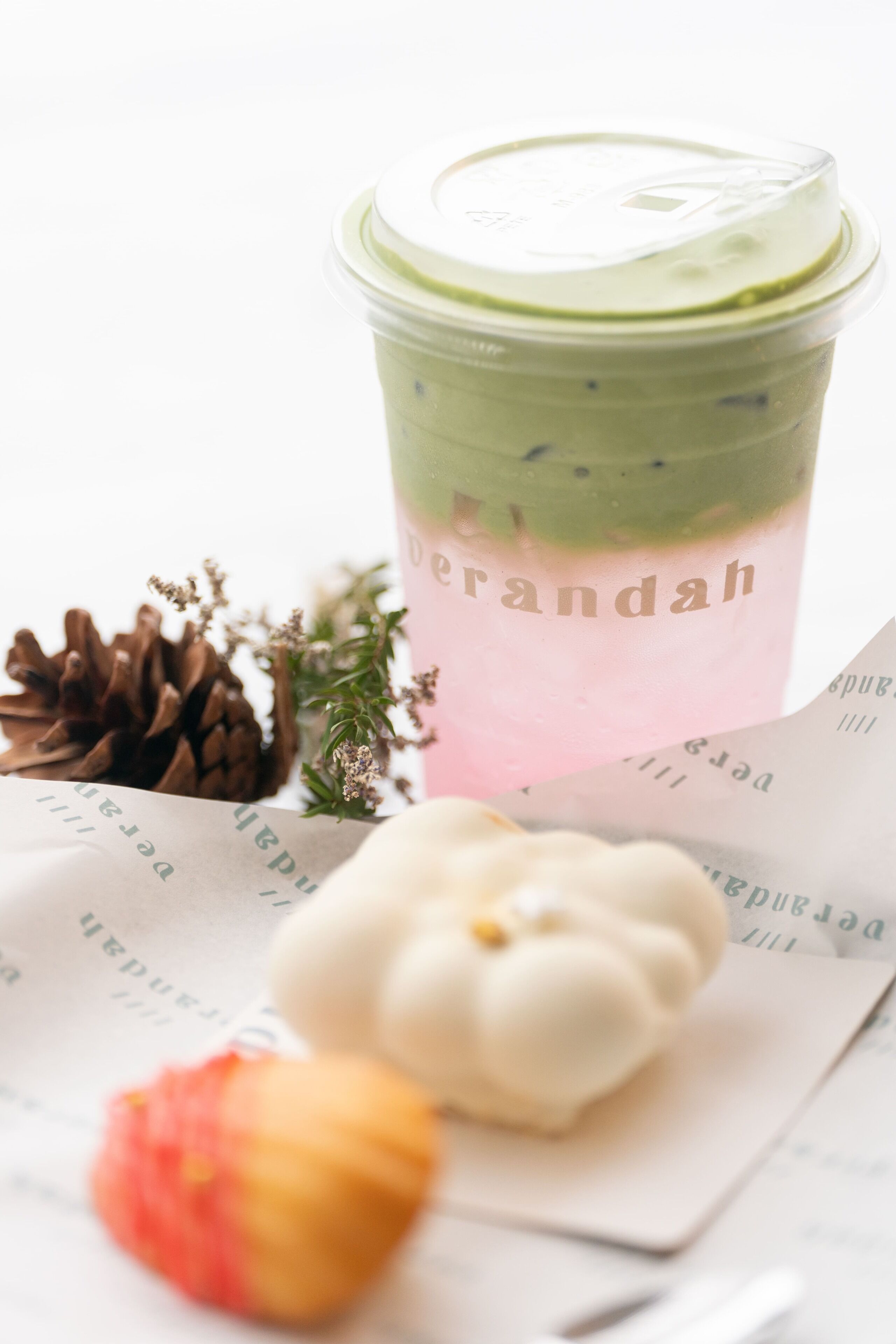 A beverage in a clear cup with a lid, a pine cone, and a small decorative item on a surface.
