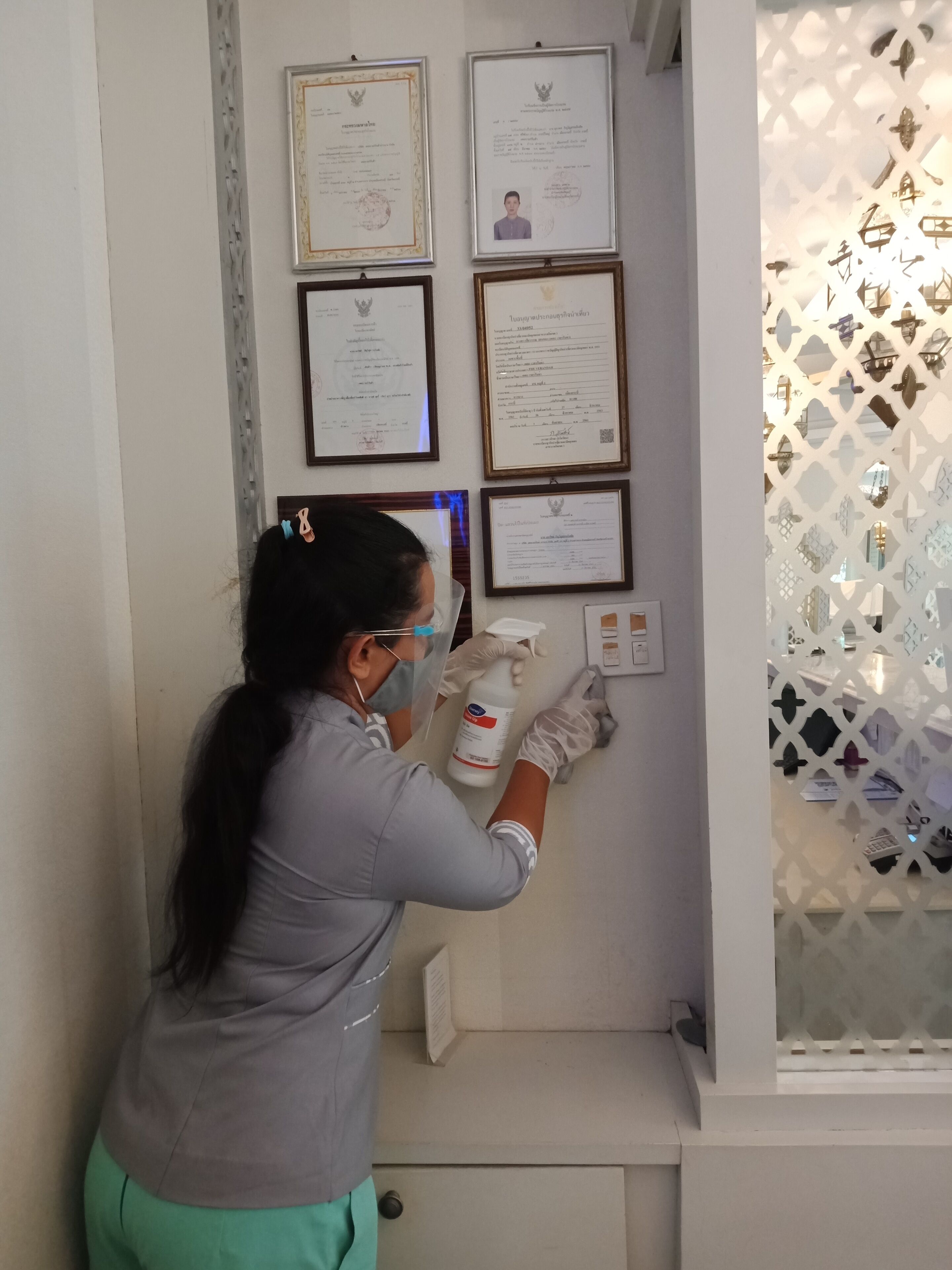 A person in a medical uniform applying a disinfectant to a wall-mounted panel.