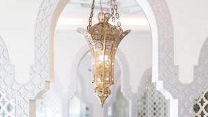 A chandelier with intricate metalwork hanging from an arched white structure. A potted plant with white flowers is placed on a marble table. - The Verandah (Krabi)