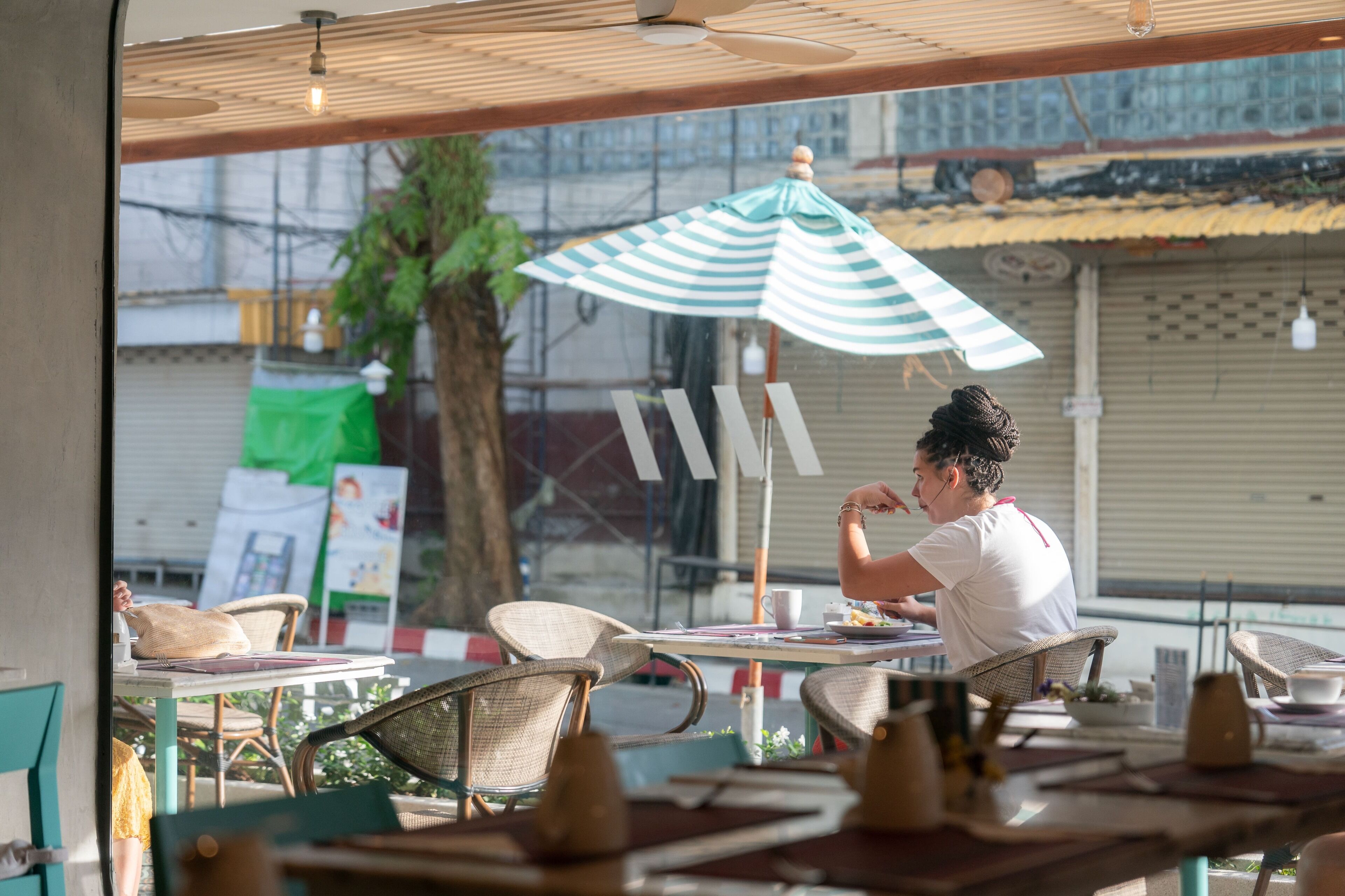 An outdoor cafe with wicker chairs and tables, a striped umbrella, and a view of the street.