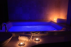 Un bain à remous avec un éclairage bleu, un lavabo et des bougies.
