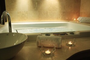A bathroom with a bathtub, a sink, and a glass candle holder with a lit candle. - Axsur Design Hotel (Montevideo)