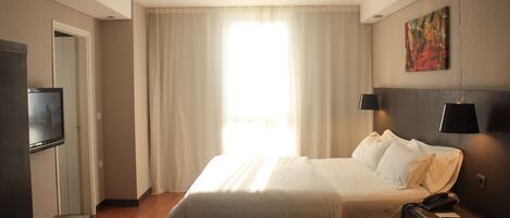 Habitación de hotel con una cama, un televisor, una mesa con dos copas de vino y un cuadro en la pared.