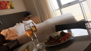 Ein Hotelzimmer mit einem Bett, einem Nachttisch mit einem Weinglas, einer Obstplatte und einem Bild an der Wand.