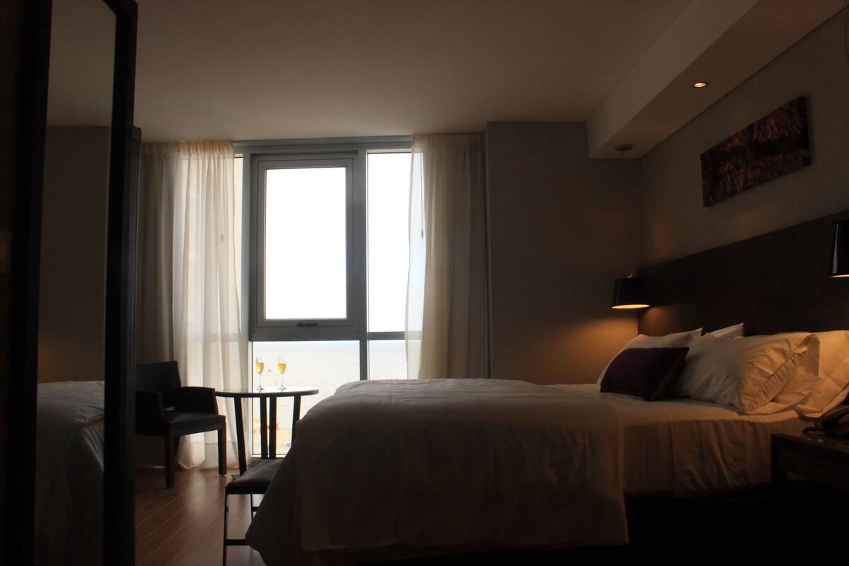 Habitación de hotel con cama, una silla, una mesita y una ventana con cortinas.