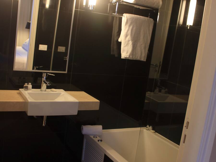 A modern bathroom with a white sink, a large mirror, a towel rack, and a bathtub.