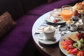 Une table ronde dressée pour le petit-déjeuner, avec une tasse de café, un verre de jus d’orange et une assiette de fruits.