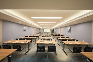 Una sala conferenze con file di tavoli e sedie, dotata di bottiglie d'acqua e bloc notes.